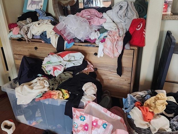 Cluttered dresser with clothes piled on top and overflowing drawers