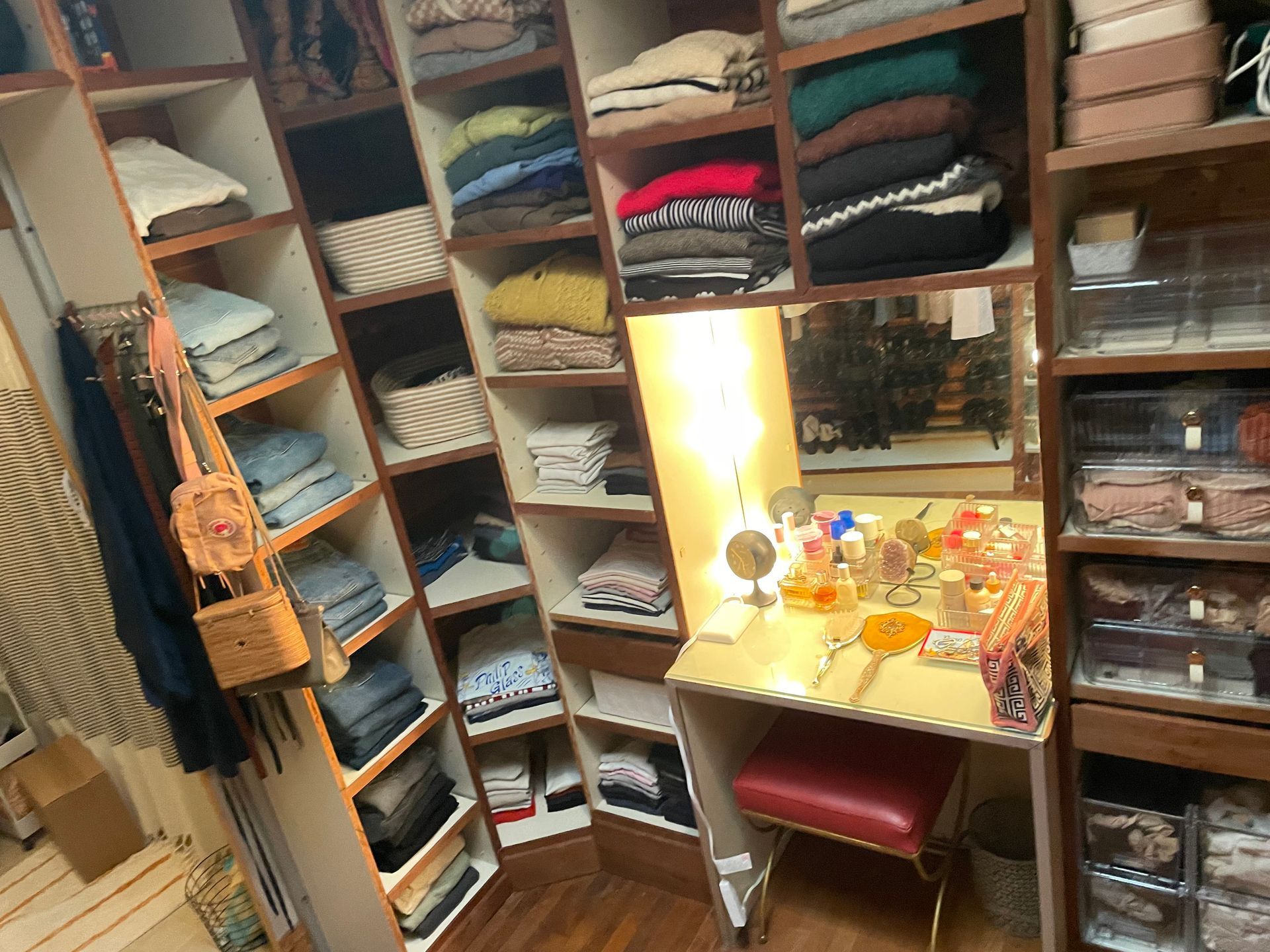 Walk-in closet with folded clothes on wooden shelves and vanity